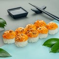 Baked sushi roll with mussels, cream cheese and spicy sauce. Decorated with greenery. In the background is a gravy boat and