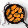 Baked sweet potatoes with rosemary in a cast-iron frying pan on a white background, top view