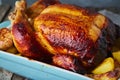 Baked whole chicken in blue casserole on dark gray old wooden table, roasted meat with potatoes. Side view, close up