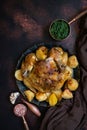 Baked whole chicken with potatoes served on a vintage plate with spinach, sea salt, garlic and shallot. Dark background, top view.