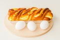 Baked yeast cake staffed with cream cheese - traditional French Brioche, and white eggs close up on wooden serving board on white Royalty Free Stock Photo