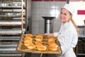 Baker in bakehouse or bakery posing with tray of fresh bread