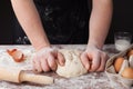 Baker in black apron prepares the dough on a wooden table, male hands knead the dough with flour