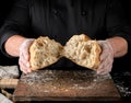 baker in black uniform broke in half a whole baked loaf of white wheat flour bread Royalty Free Stock Photo