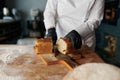 Baker chef holding knife and cutting fresh bread on wooden table