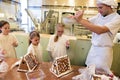 Gingerbread house baking in the run up to Christmas. Baker shows children how to sprinkle powdered sugar over gingerbread house