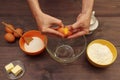 Baker hands break an egg over a bowl on wooden table