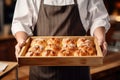 A baker holding a tray of freshly baked buns.