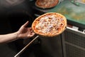 A baker holds pizza on a shovel for baking. top view on hands and pizza.