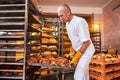 Baker holds a tray with fresh hot bread in his hands against background of shelves with pastries in bakery. Industrial production Royalty Free Stock Photo