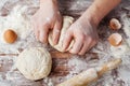 Baker prepares the dough on a wooden table, male hands knead the dough with flour