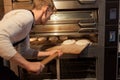 Baker putting dough into bread oven at bakery