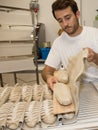 Baker putting unbaked bread dough into hot oven in bakery