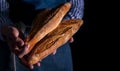 Baker`s hands hold fresh bread over dark background