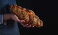 Baker`s hands hold fresh bread over dark background