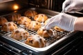 Baker& x27;s skilled hands placing hot cross buns into the preheated oven