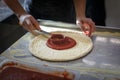 Baker is smearing base of pizza with tomato sauce in the kitchen in a restaurant