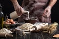 Baker in uniform pouring milk from plastic bottle into bowl. A handful of flour with egg on a rustic kitchen. Royalty Free Stock Photo