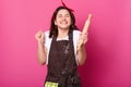 Baker woman holds baking rolling pin, wears brown apron, white t shirt. Young girl bends elbows and shouts yes with closed eyes,