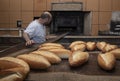 Baker. A young handsome bakery worker on the background of bread, takes bread from a stove with a wooden shovel. Industrial Royalty Free Stock Photo