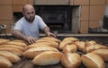 Baker. A young handsome bakery worker on the background of bread, takes bread from a stove with a wooden shovel. Industrial Royalty Free Stock Photo