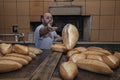 Baker. A young handsome bakery worker on the background of bread, takes bread from a stove with a wooden shovel. Industrial Royalty Free Stock Photo