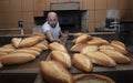 Baker. A young handsome bakery worker on the background of bread, takes bread from a stove with a wooden shovel. Industrial Royalty Free Stock Photo