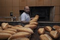 Baker. A young handsome bakery worker on the background of bread, takes bread from a stove with a wooden shovel. Industrial Royalty Free Stock Photo