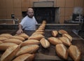 Baker. A young handsome bakery worker on the background of bread, takes bread from a stove with a wooden shovel. Industrial Royalty Free Stock Photo