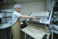 At the bakery: baker standing at a dough forming machine and forming dough for baking baguette