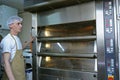 At the bakery: baker standing near an electric oven watching temperature on a control panel