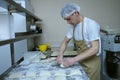 At the bakery: baker standing at a work table and molding dough for baking bread