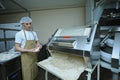 At the bakery: baker working a dough forming machine forming dough for baking baguette