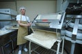 At the bakery: baker working a dough forming machine forming dough for baking baguette