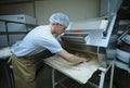 At the bakery: baker working a dough forming machine forming dough for baking baguette