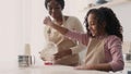 Bakery preparations. Cute little black girl flouring tabletop at kitchen, cooking cookies with mother together