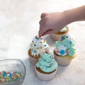 A child`s hand decorates cooked cupcakes with cream. Bakery products. A square picture.