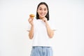 Bakery and sweets. Happy asian woman looking at tasty cupcake, eating pastry, white background