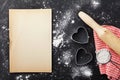 Baking background with flour, rolling pin, paper sheet and heart shape on kitchen black table from above for Valentines day.