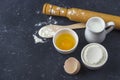 Baking background. Ingredients and utensils for cooking cake flour, egg, milk, sugar, rolling pin, wooden spoon on dark table. Royalty Free Stock Photo