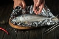 Before baking, fresh fish must be wrapped in foil and aromatic spices and peppers must be added. Close-up of chef hands while Royalty Free Stock Photo