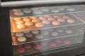 Baking macaroons in the oven. Colorful macarons cookies on baking trays in the oven. The process of making cookies in a