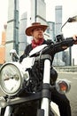 Portrait of stylish male dressed in a black leather jacket and bandana sitting on his custom-made retro motorcycle Royalty Free Stock Photo