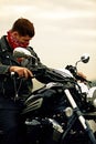 Portrait of stylish male dressed in a black leather jacket and bandana sitting on his custom-made retro motorcycle Royalty Free Stock Photo