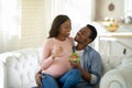 Balanced diet in pregnancy concept. Handsome black man giving his lovely expectant wife yummy vegetable salad indoors Royalty Free Stock Photo