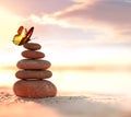 Balanced pebble pyramid and butterfly on the beach. Abstract warm sunset bokeh with sand on the background. Zen stones Royalty Free Stock Photo