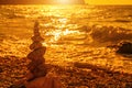 Balanced pebble pyramid on the beach on a sunset time. Sea waves and foam on the background. Selective focus. Zen stones on the Royalty Free Stock Photo