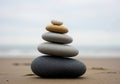 A balanced stack of five smooth stones is arranged on a sandy beach. The stones vary in color and Royalty Free Stock Photo