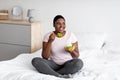 Balanced weight loss diet concept. Plus size Afro woman eating vegetable salad, sitting on bed at home Royalty Free Stock Photo