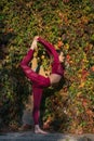 Balancing girl in red sportswear doing yoga pose on the alley in the autumn park